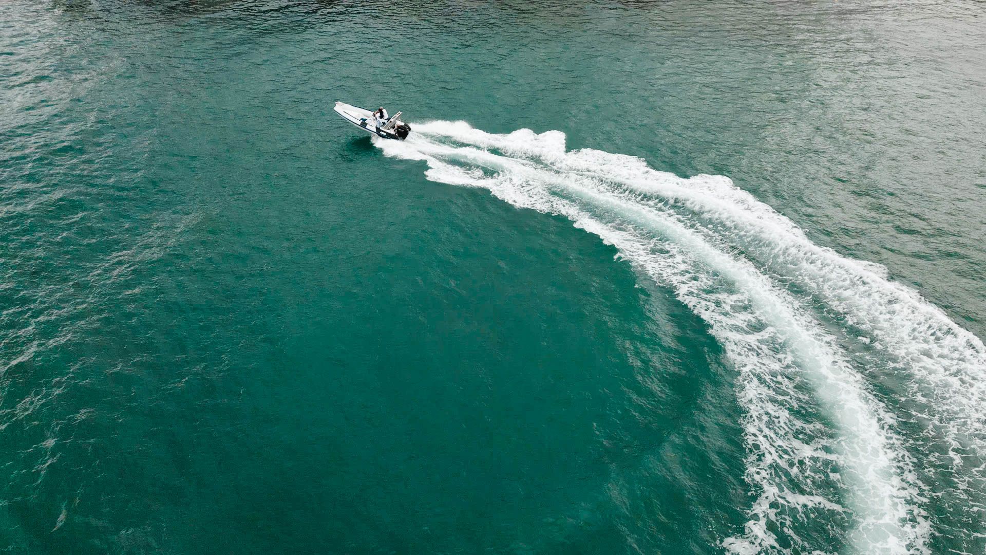 Aerial view of a speedboat making a sharp turn in turquoise waters leaving white wake patterns.