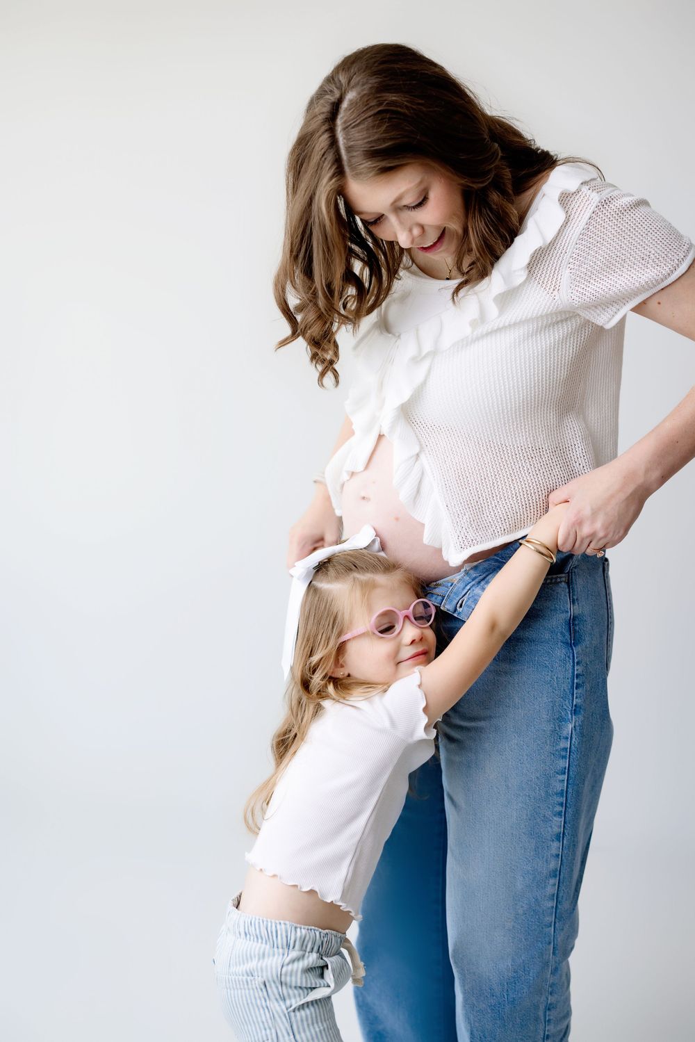 A heartwarming moment between a pregnant woman and young child in matching white tops and denim.