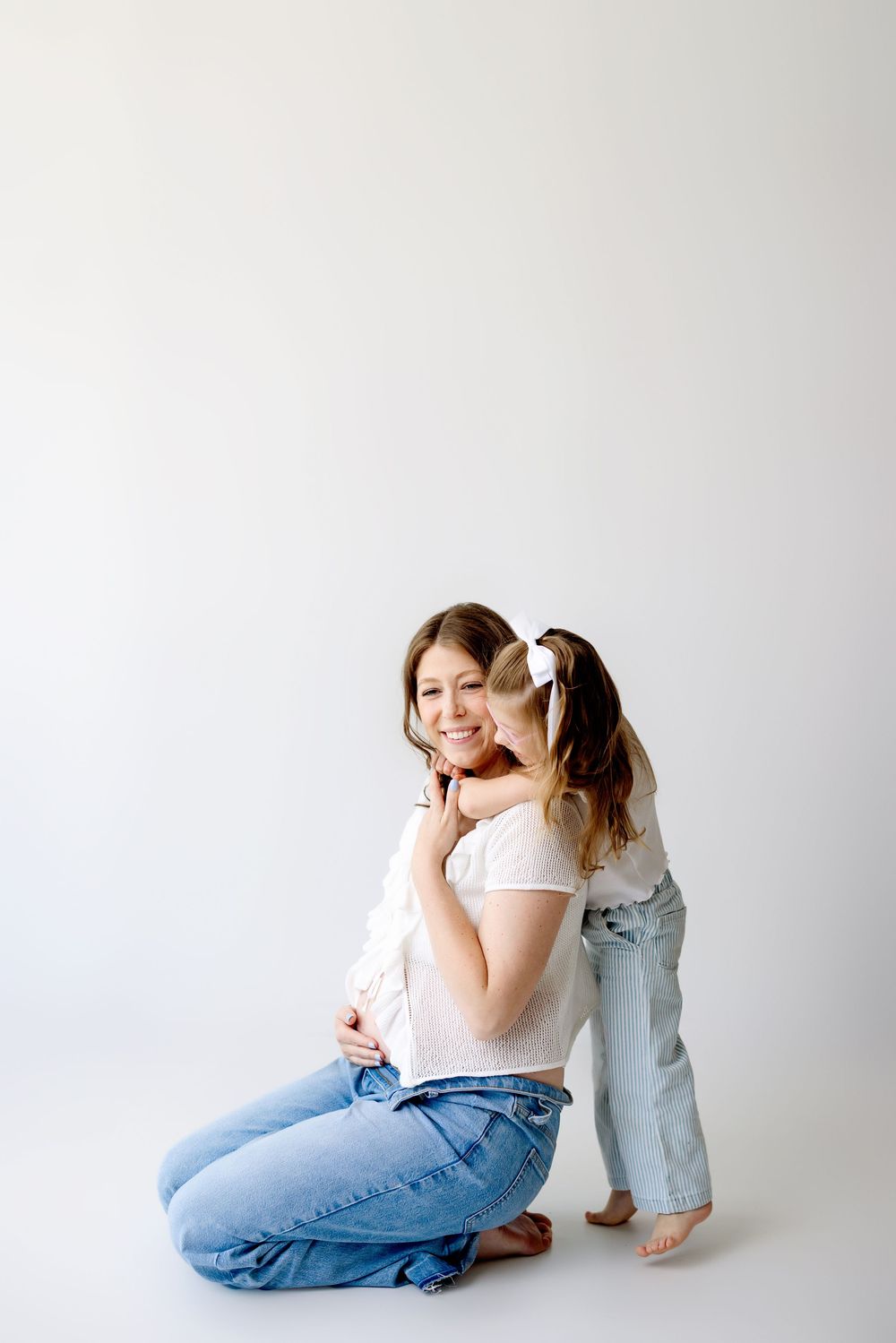 A tender moment captured against a white backdrop as they embrace while wearing casual denim and white tops.