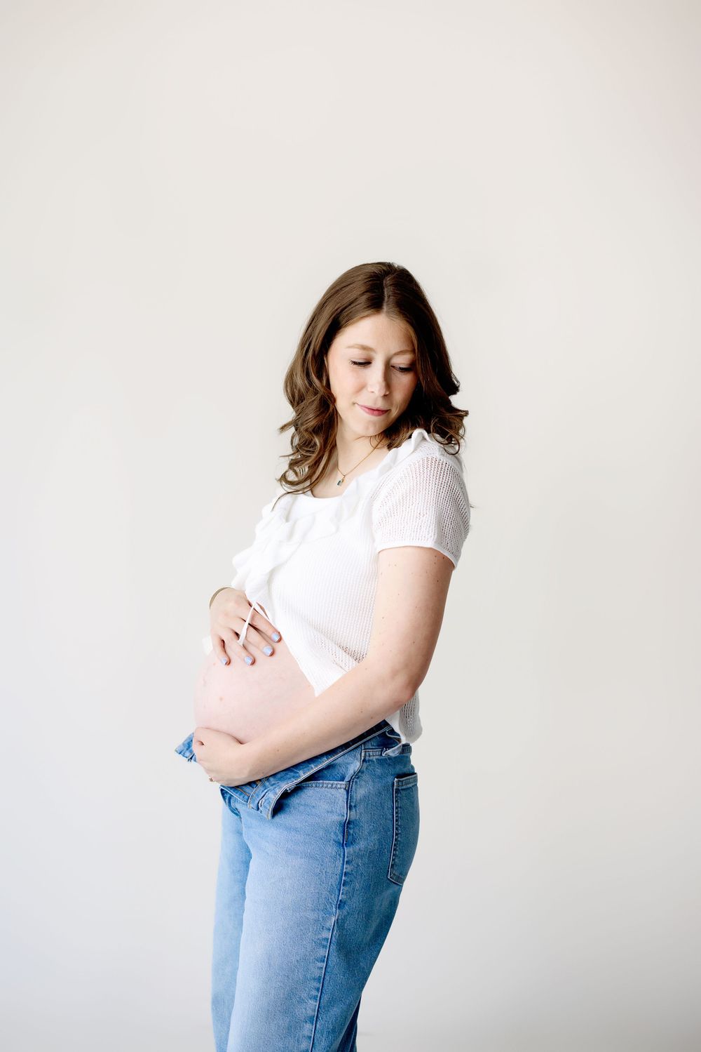 Side view of someone wearing a white t-shirt and jeans looking down at their midsection against a neutral background.