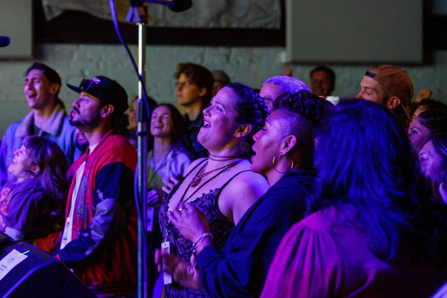 Concert audience bathed in purple lighting watches a performance with expressions of joy and excitement.