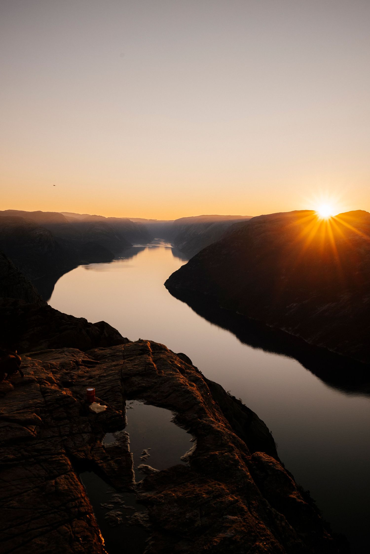 Scenic sunset view over a winding river canyon with sunburst peeking over mountain ridges and reflective waters below.