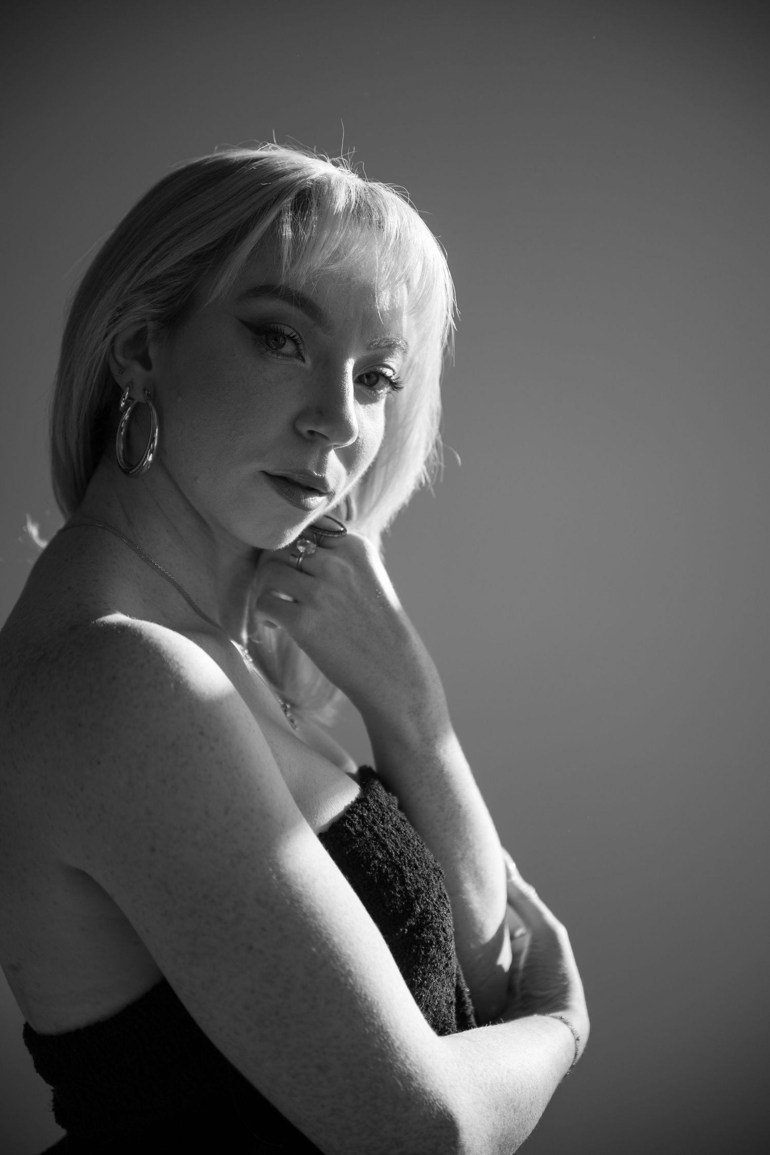 Black and white artistic portrait of person in sleeveless top looking pensively to the side against dark background.