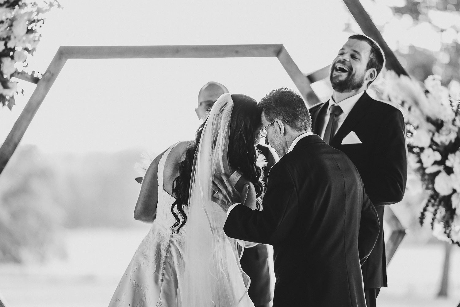 the groom laughs and smiles as his bride and her father walk down the aisle