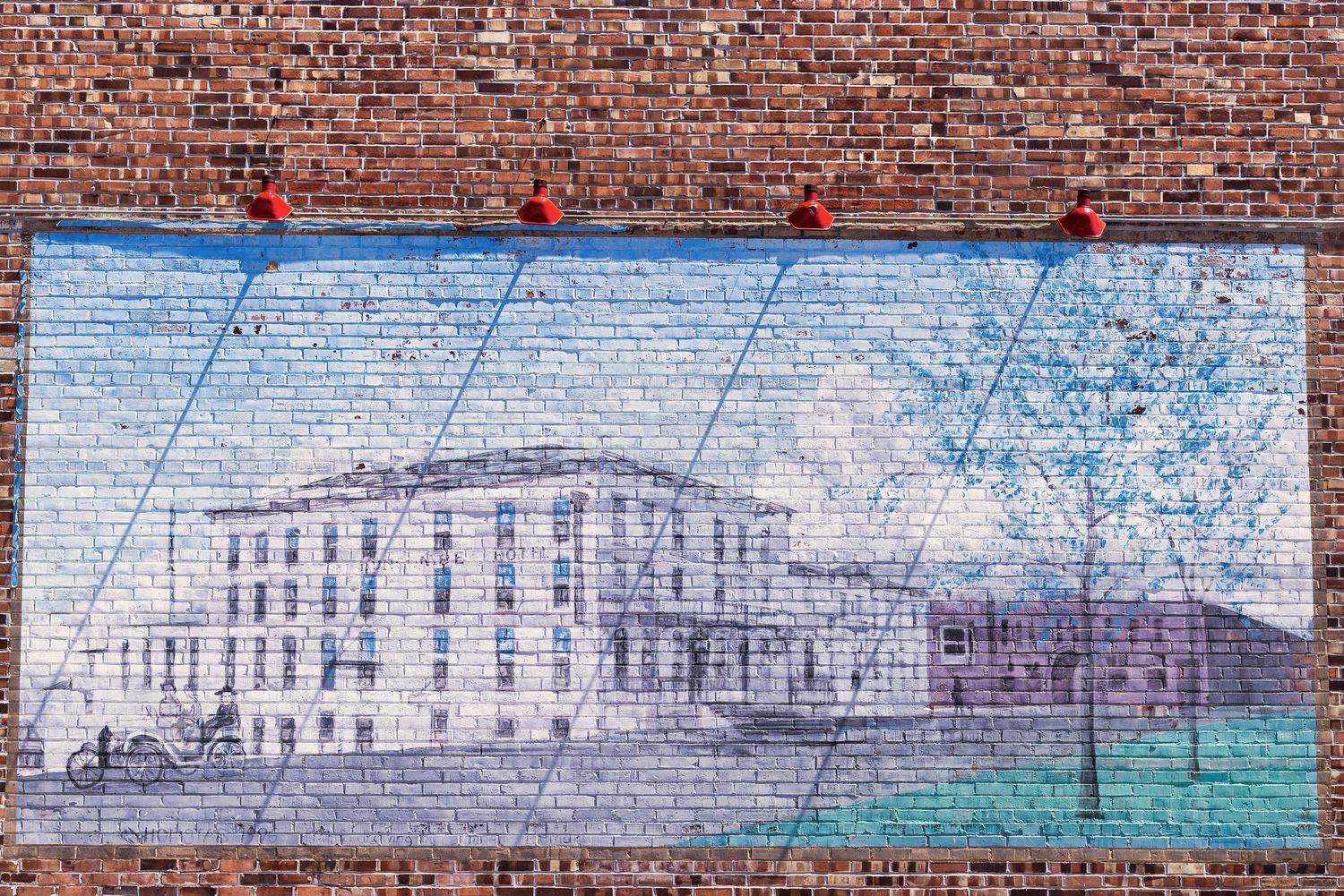 A long painted mural on a red brick wall shows an urban landscape with buildings in Downtown Fort Dodge Iowa