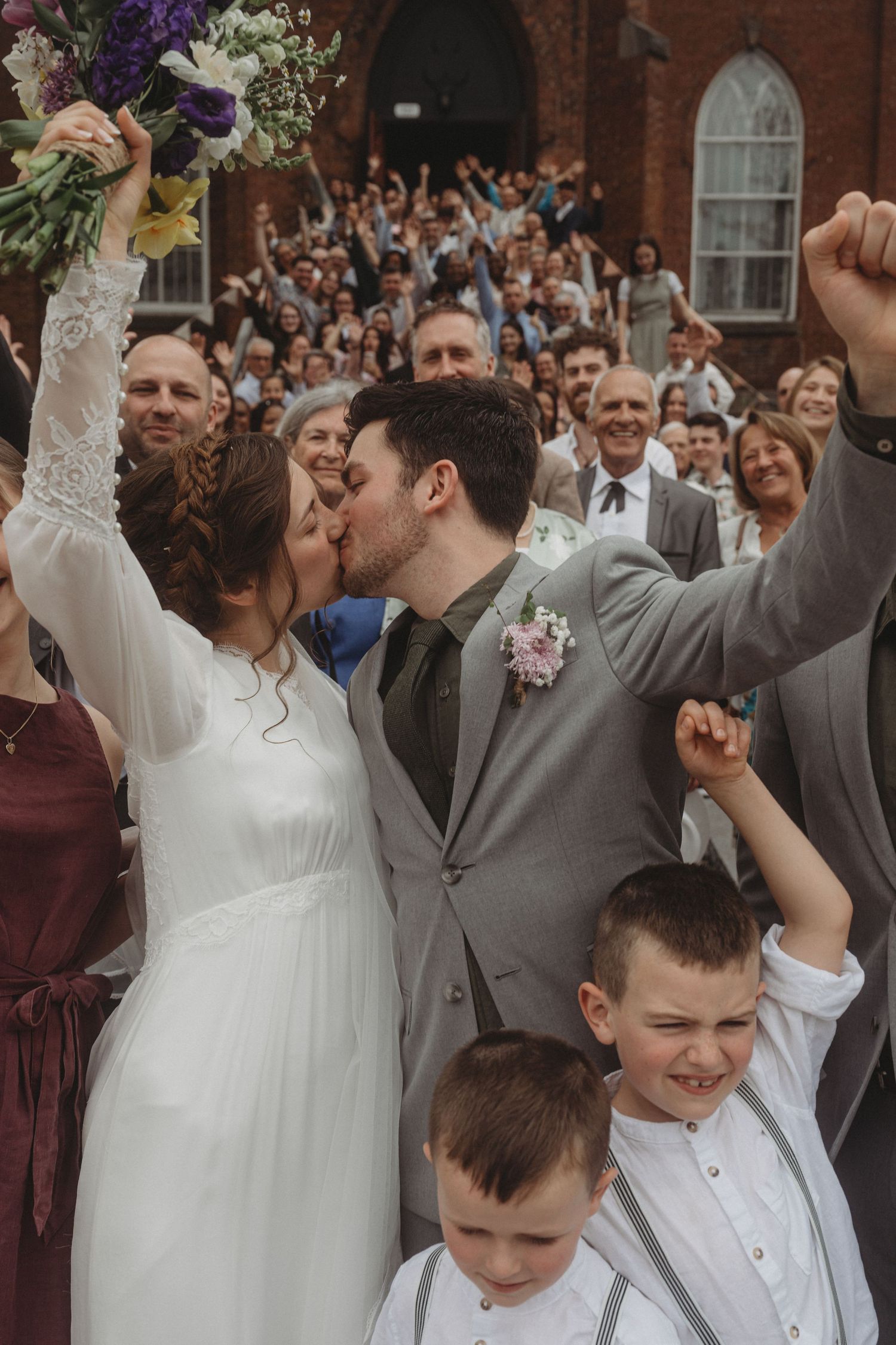 A celebratory moment outside a brick church with a crowd cheering during a wedding ceremony.