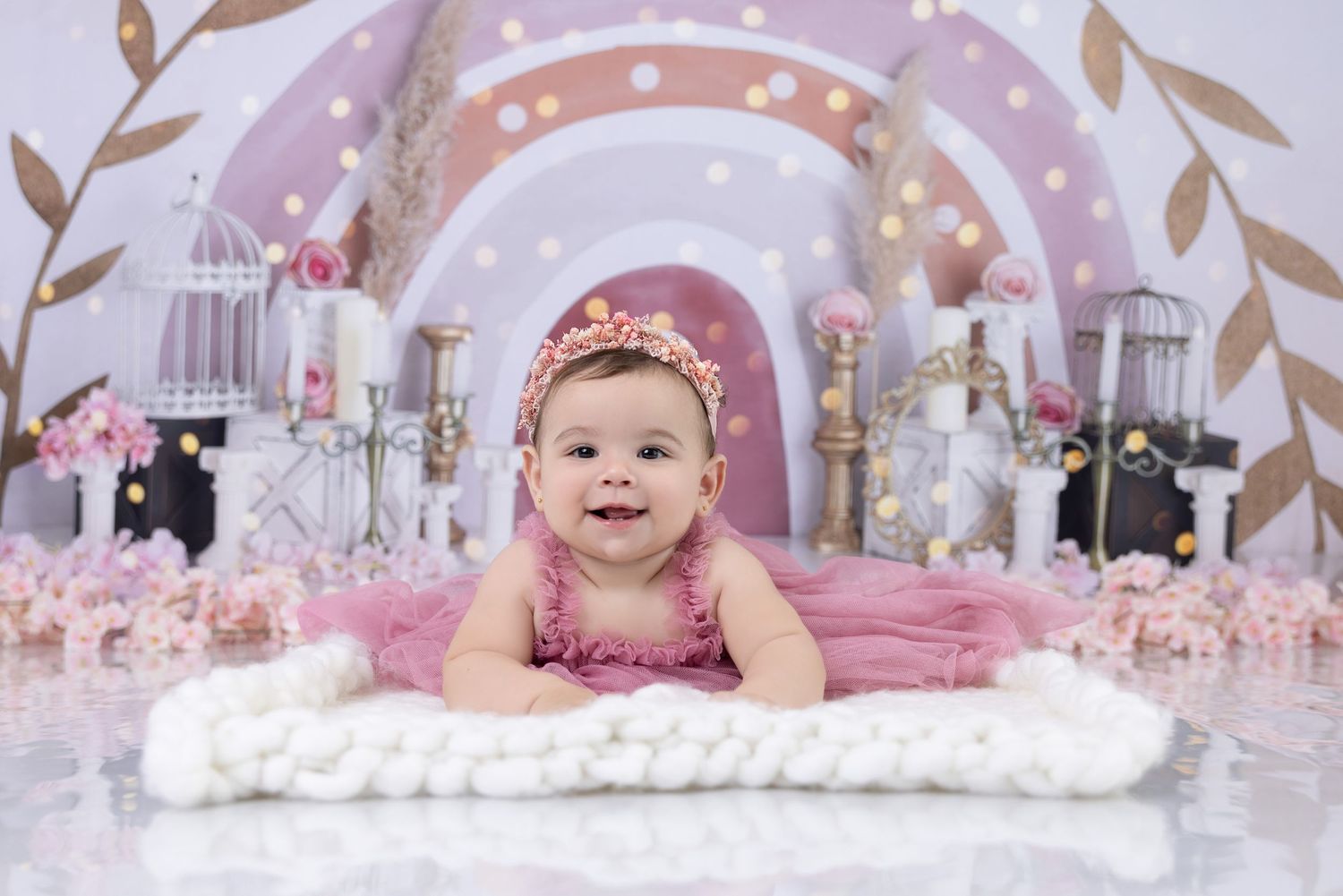 Baby in pink outfit lying on white furry rug with dreamy pink and white fantasy backdrop and arches. Milestone session.