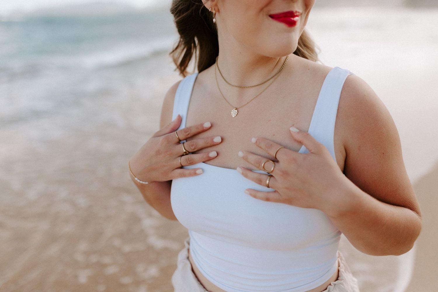 Person in white dress touching heart with both hands on sandy beach at sunset.
