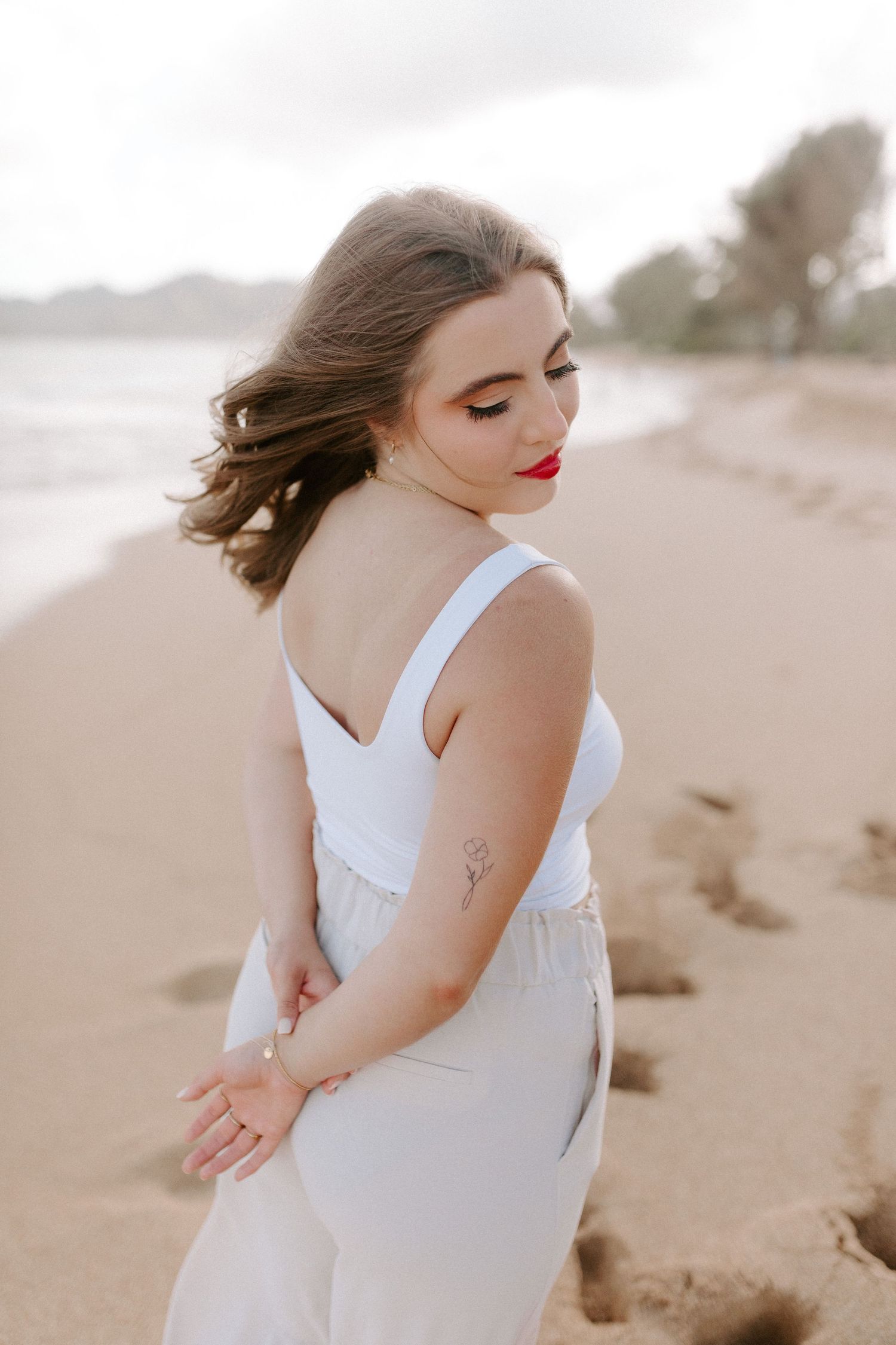 Side profile of person in white dress posing on beach with windswept hair.