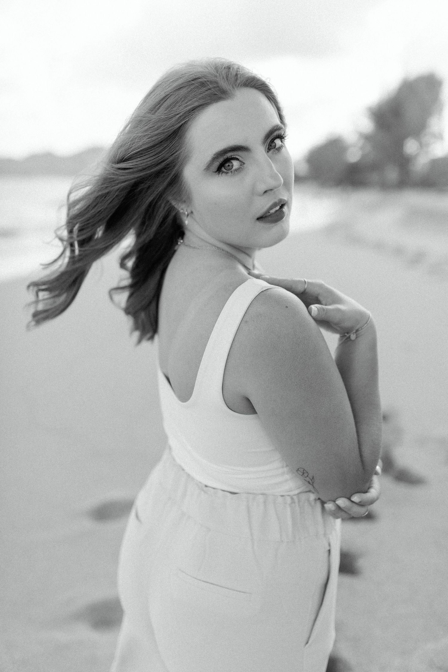 Black and white portrait of someone in white dress looking over shoulder on beach.