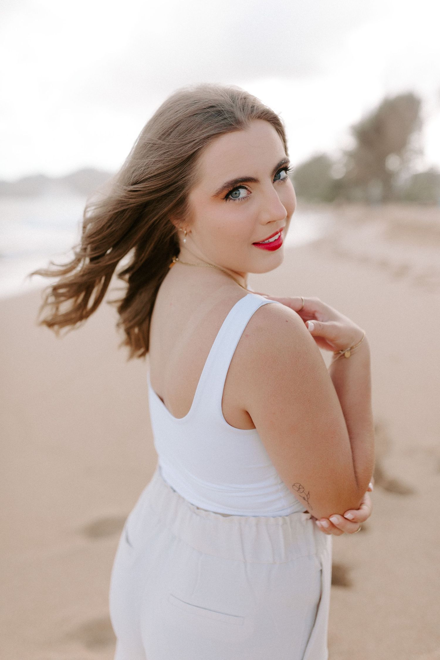 Portrait of person in white dress with windswept hair looking over shoulder on beach.