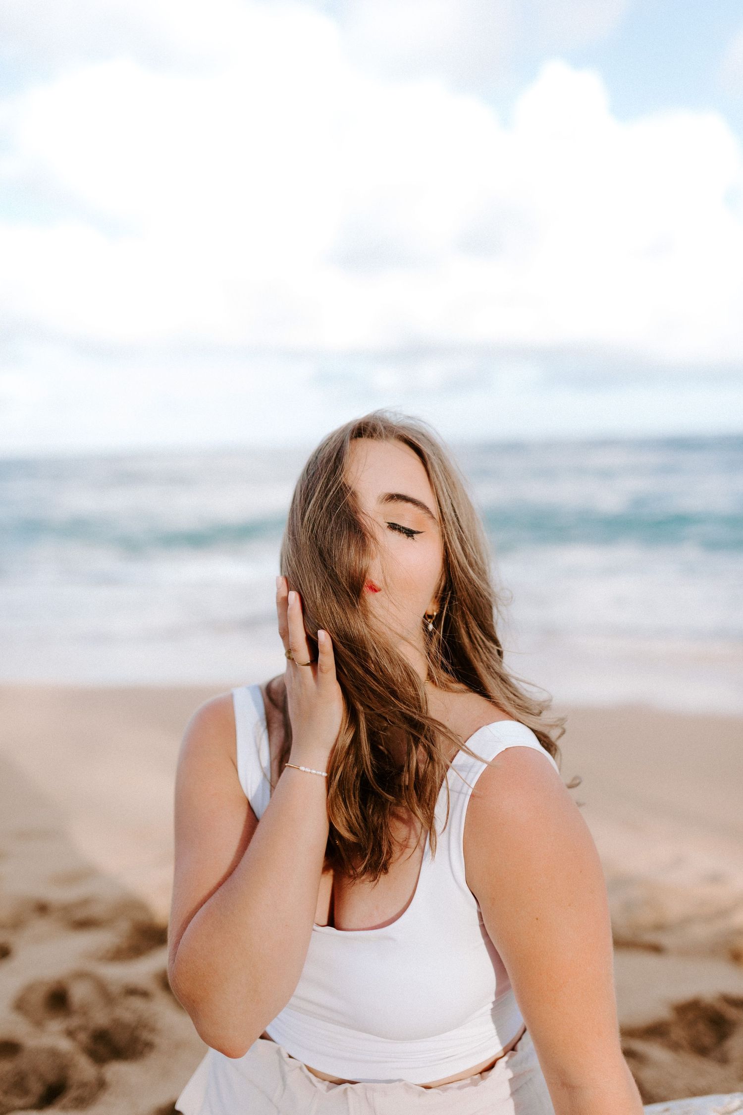 A beachside portrait featuring someone in a white tank top with flowing hair.