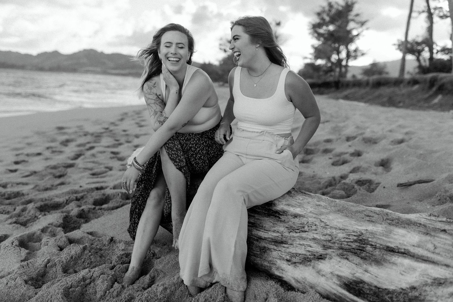 A black and white photo of two friends enjoying a moment of laughter on the beach.