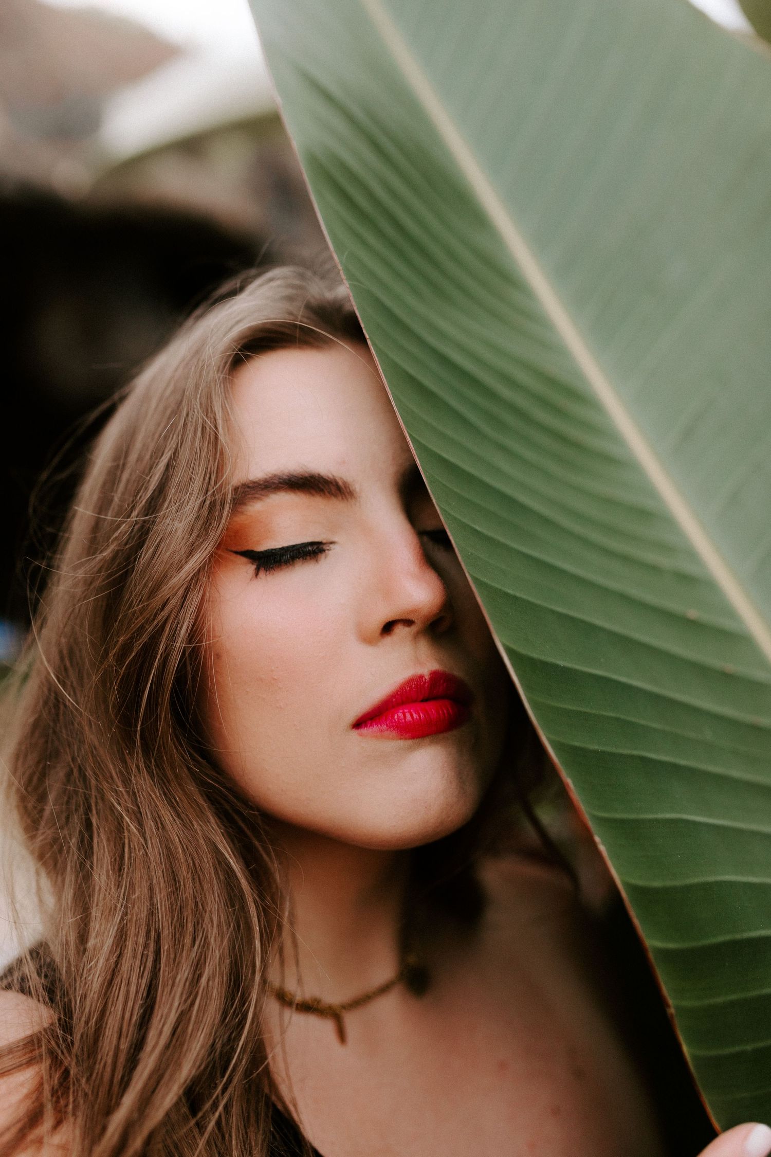Creative portrait behind a large green banana leaf with bold red lipstick.