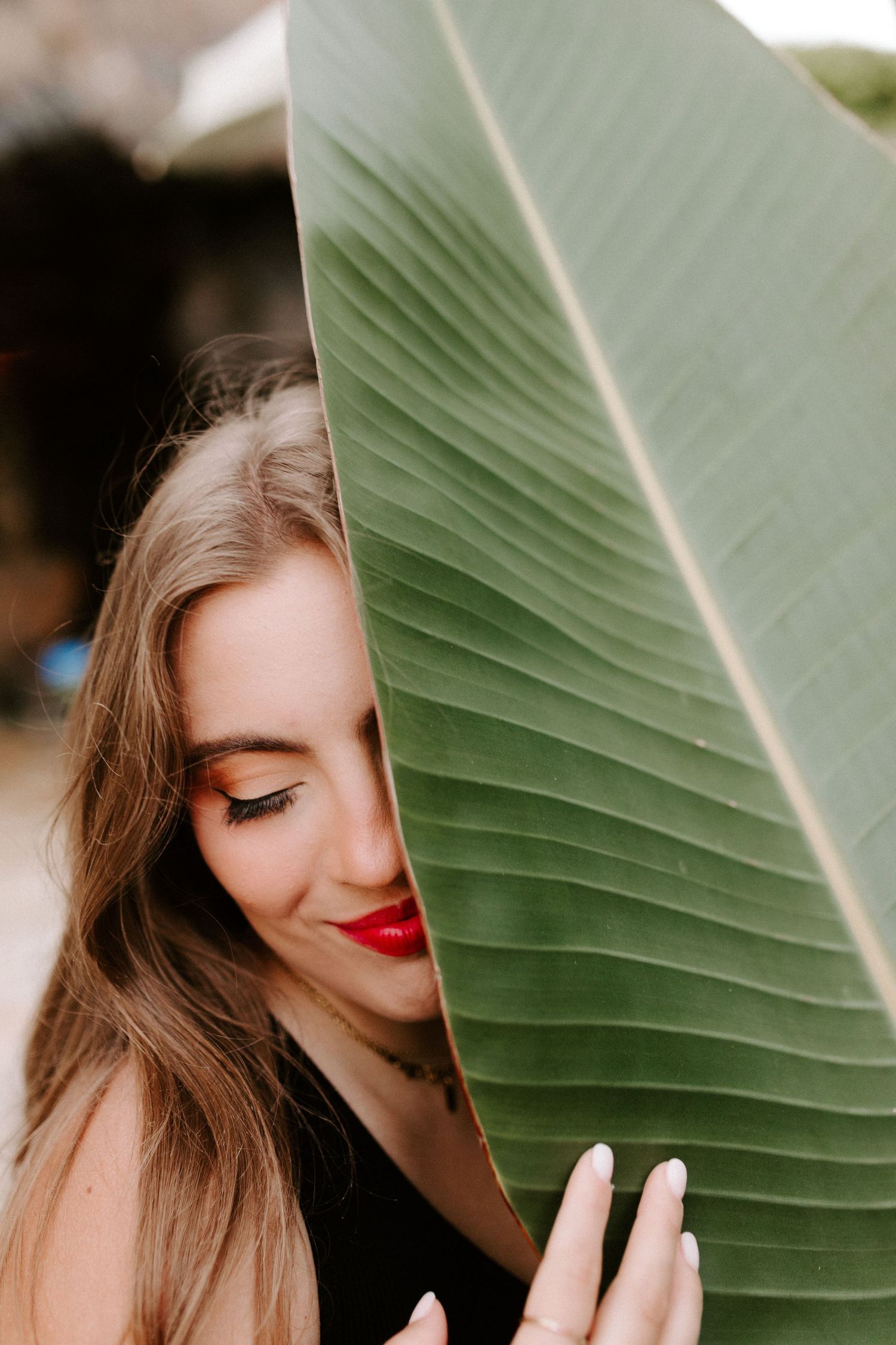 Artistic portrait peeking through tropical foliage with vibrant makeup.