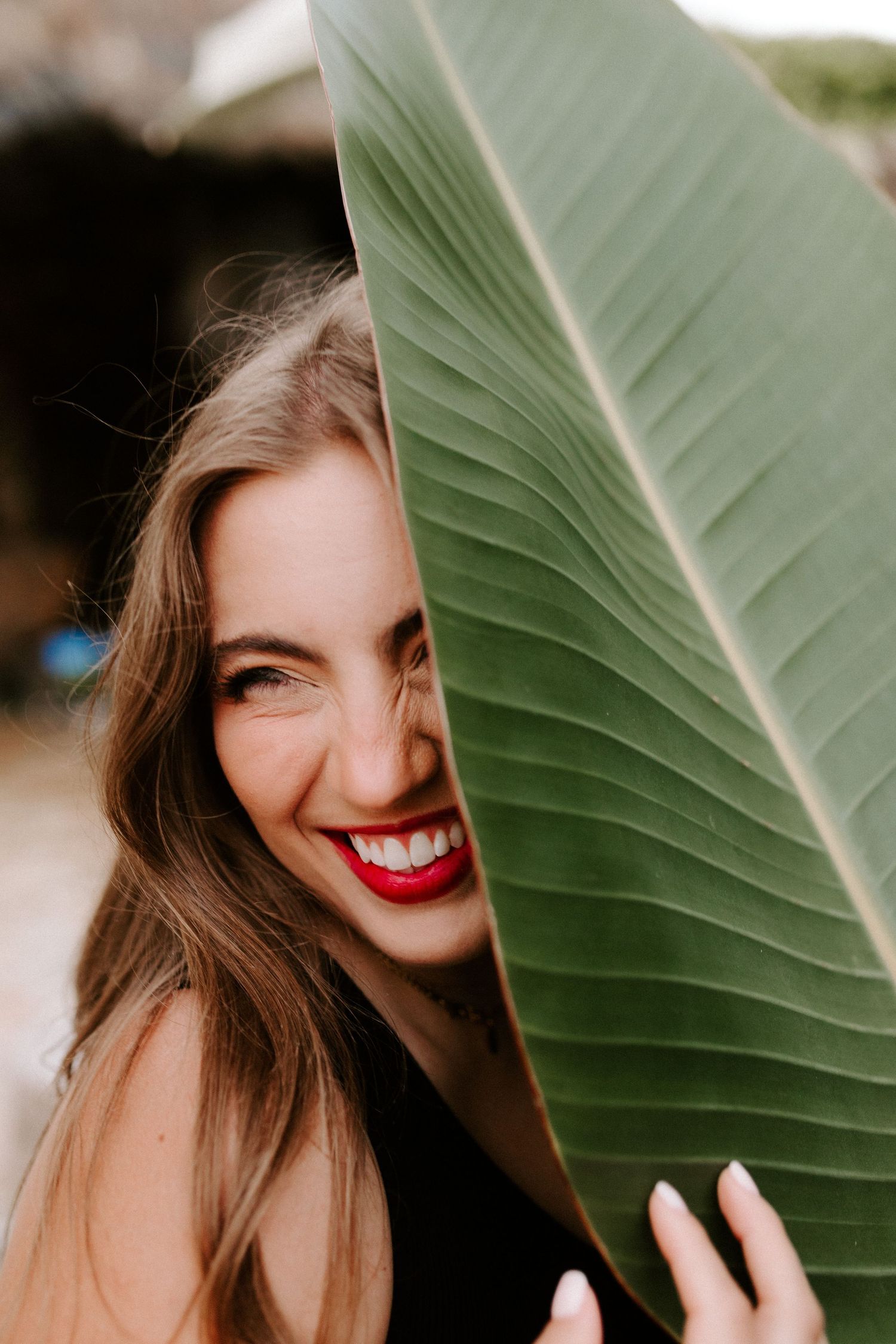 Playful tropical portrait with subject smiling behind a large green leaf.