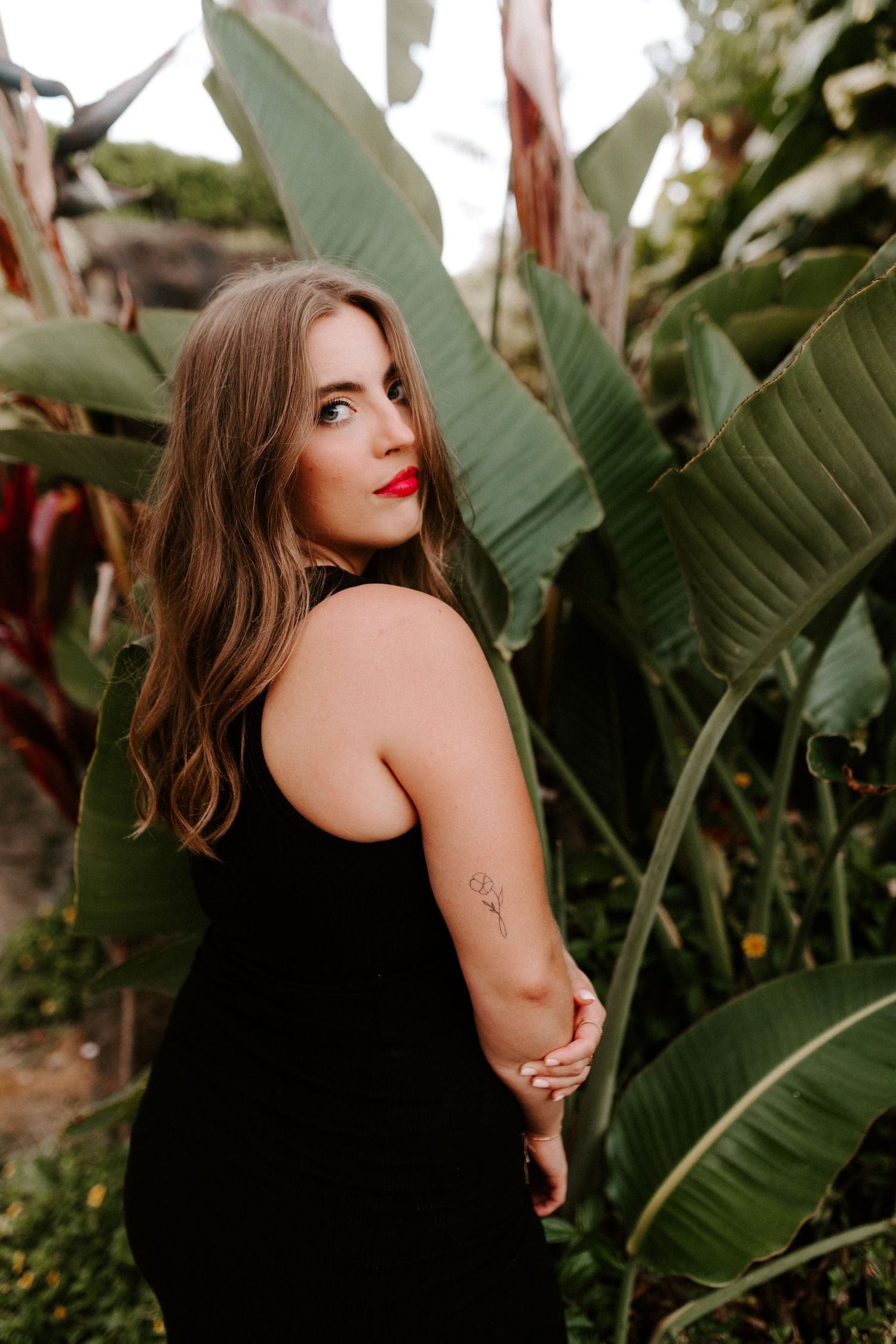 Stylish portrait in black dress among tropical banana leaves at sunset.