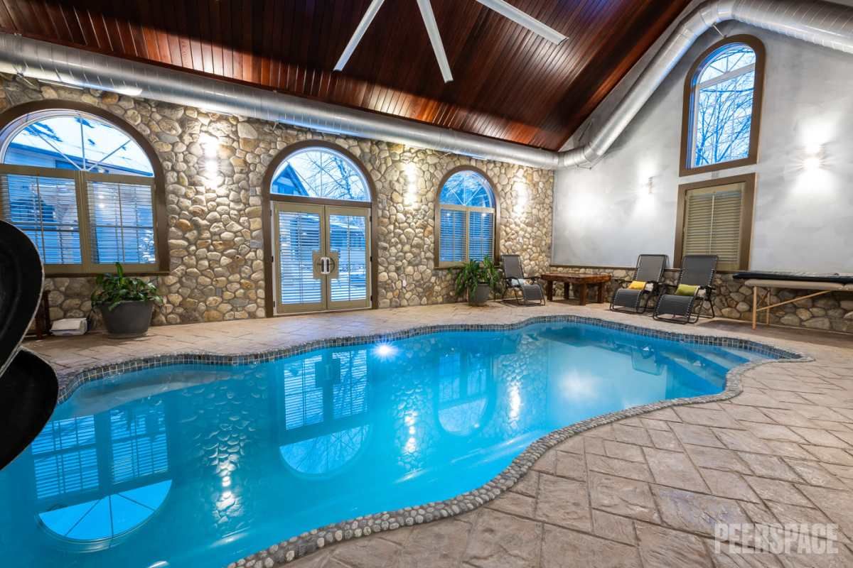 Indoor swimming pool with stone accent walls, arched windows, and wooden beam ceiling in elegant setting.