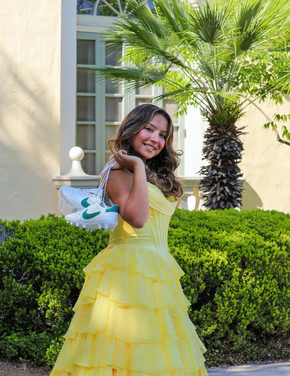 A charming yellow ruffled dress stands out against lush greenery and palm trees at a luxury resort entrance.