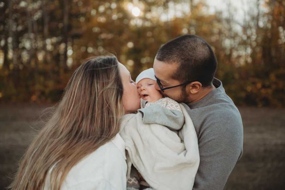 A tender family moment captured in a sunlit autumn field with warm golden tones in the background.