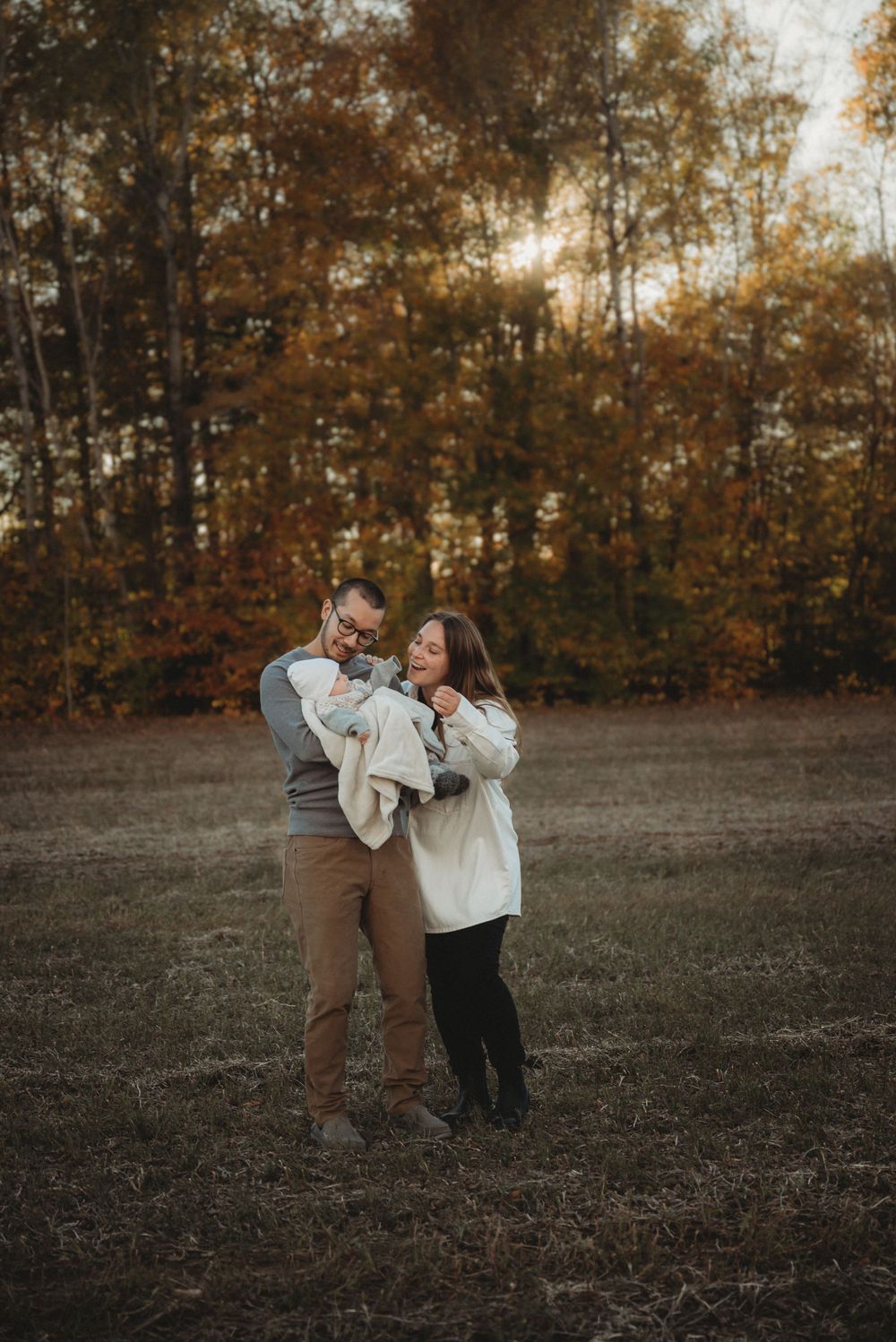 A joyful family sharing laughter together in a field surrounded by fall foliage.