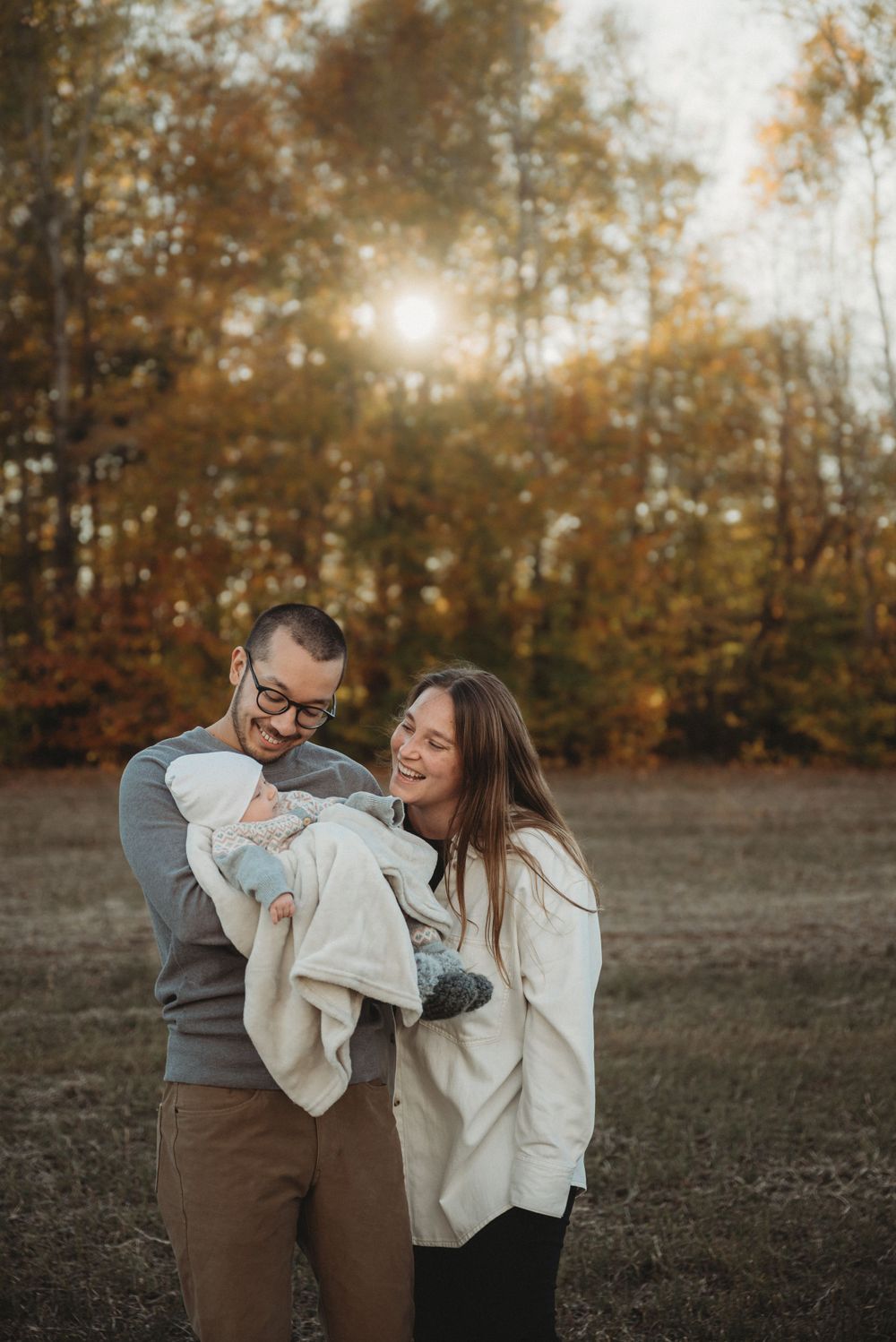 A heartwarming family portrait set against a backdrop of autumn trees with sunlight streaming through.