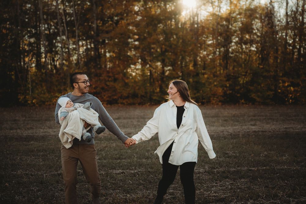 A playful family moment captured in a fall field with golden sunlight filtering through trees.