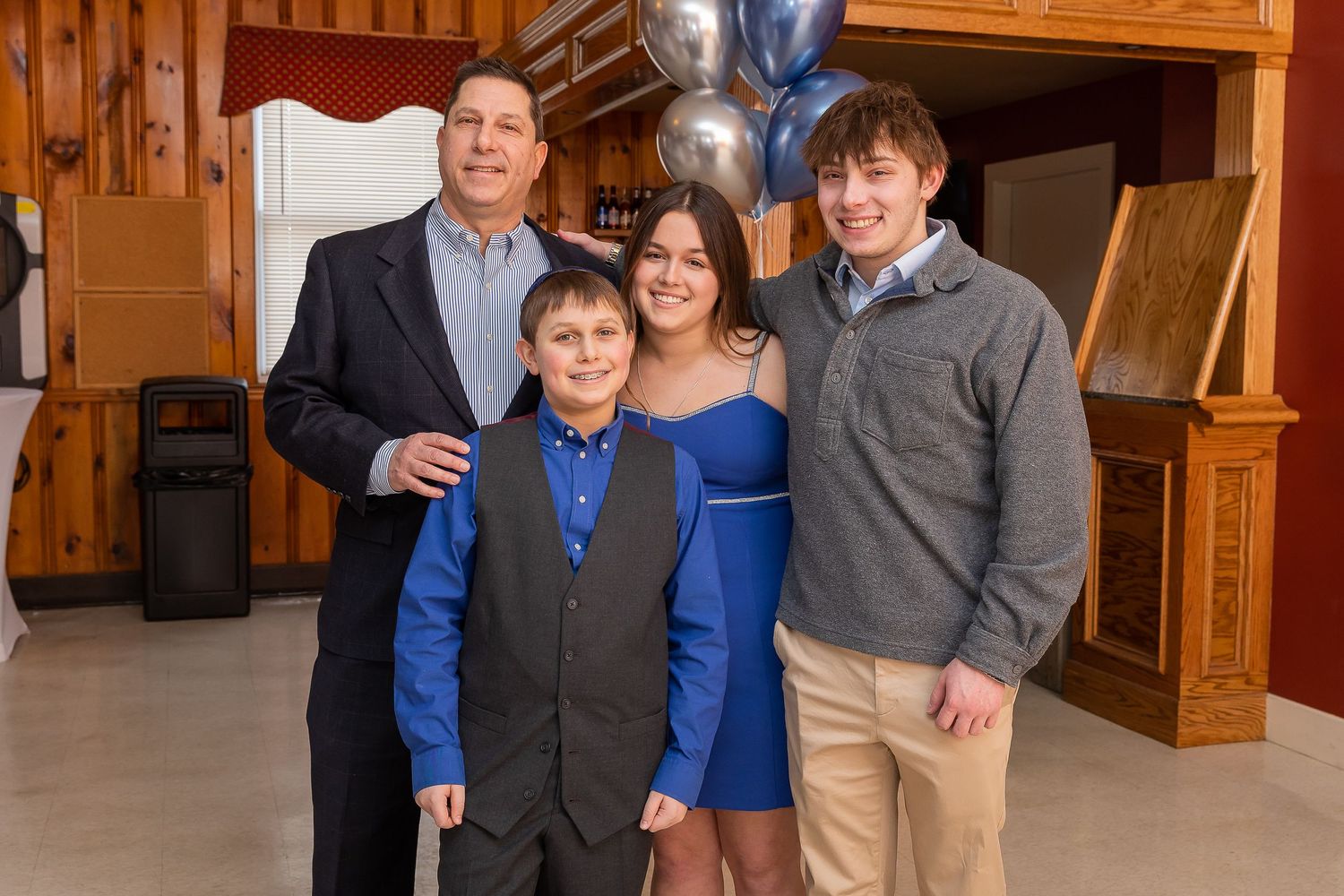 A small group poses together for a formal photo with blue balloons in the background.