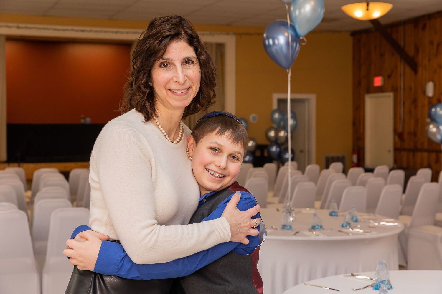 A warm embrace between two people at a formal event with white chairs in the background.