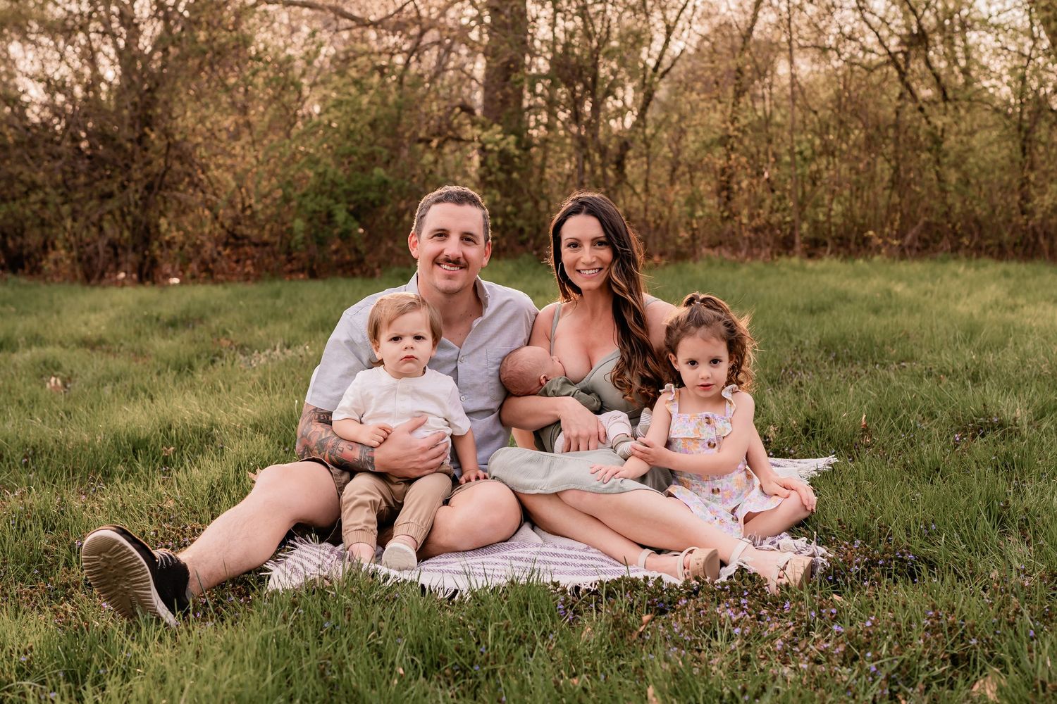 A family sitting together on a blanket in a grassy field during golden hour.