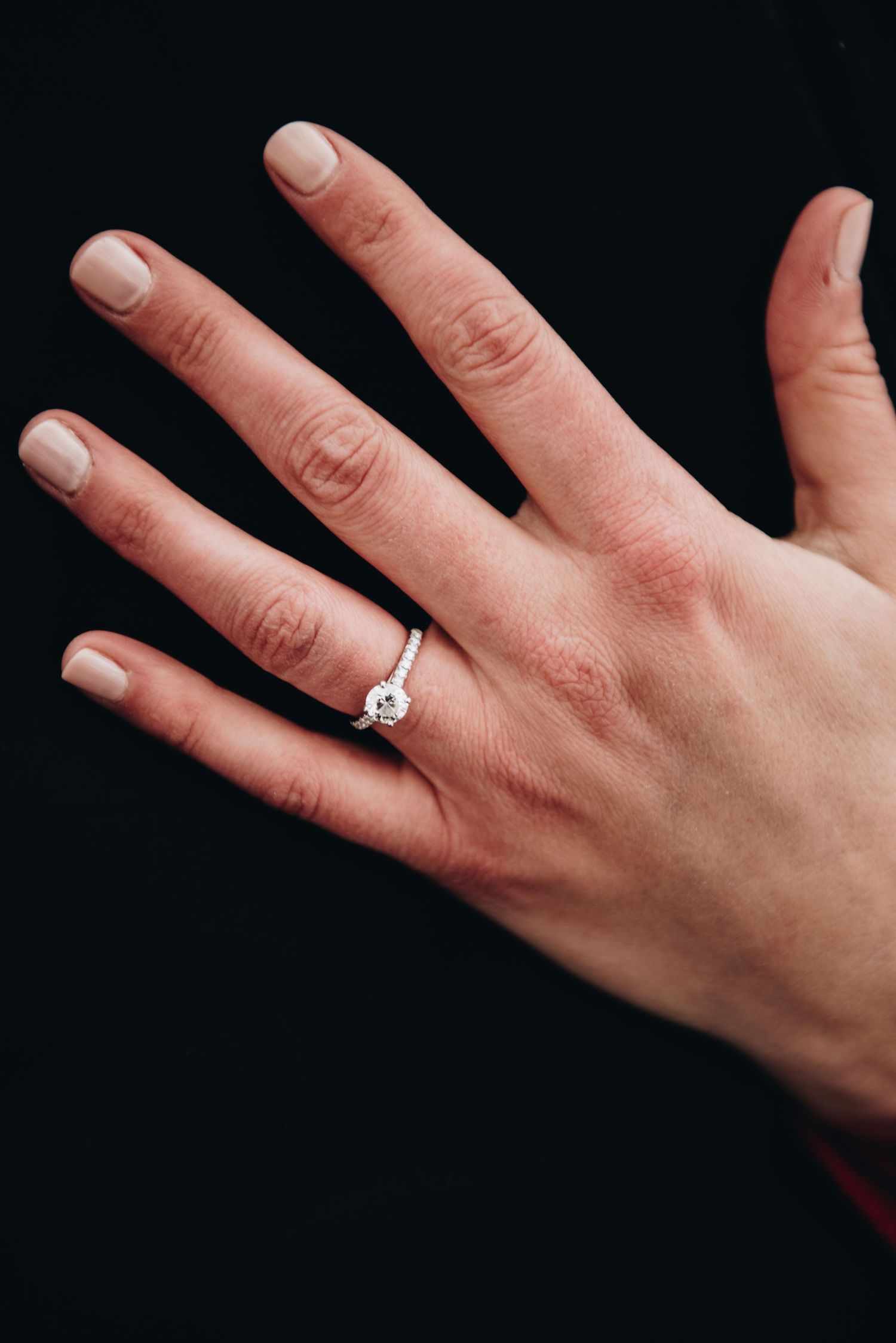 Close-up of a hand wearing an engagement ring against a black background.