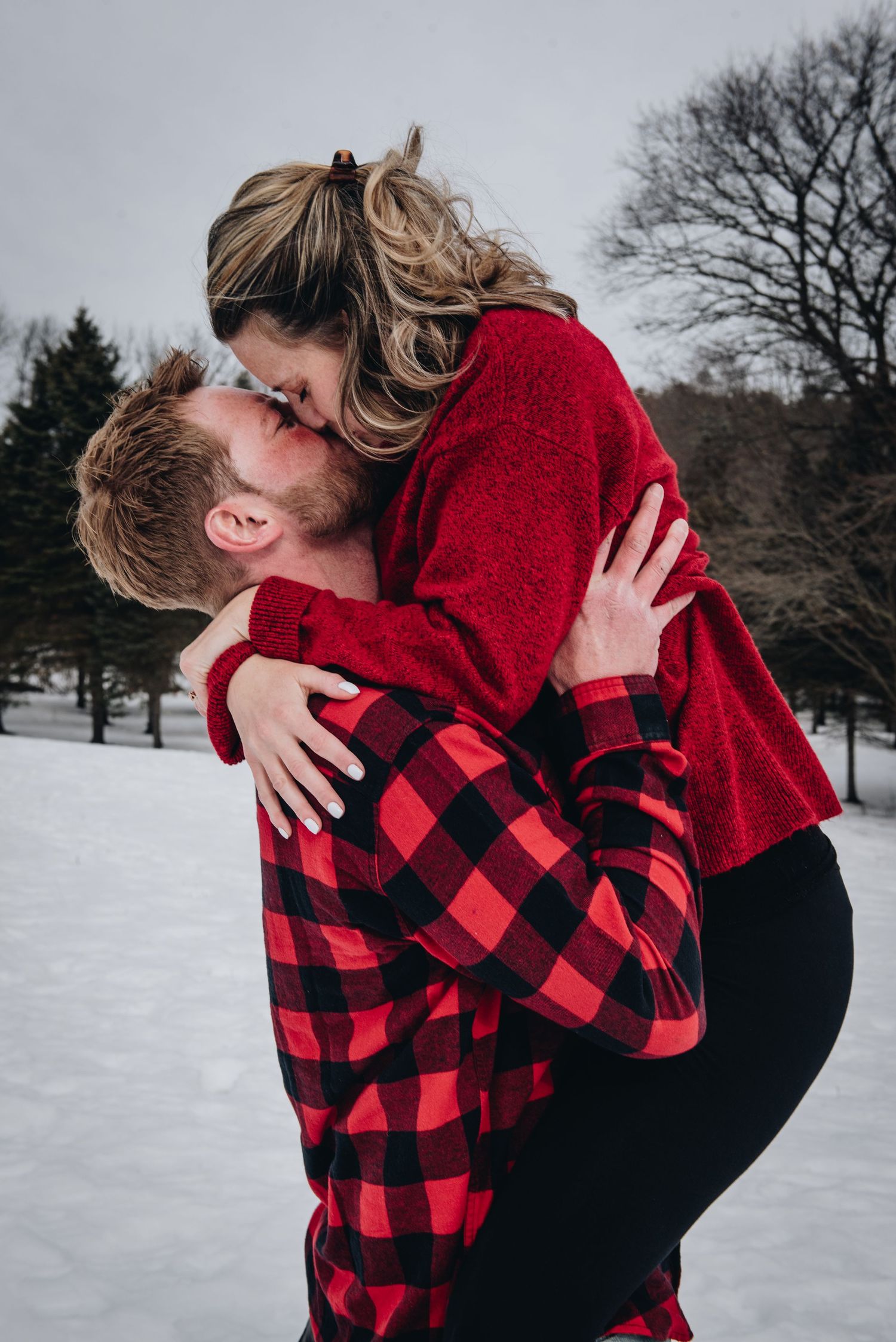A romantic winter embrace between a couple in coordinating red buffalo plaid and sweater. Massachusetts Engagement Photographer Serving New
