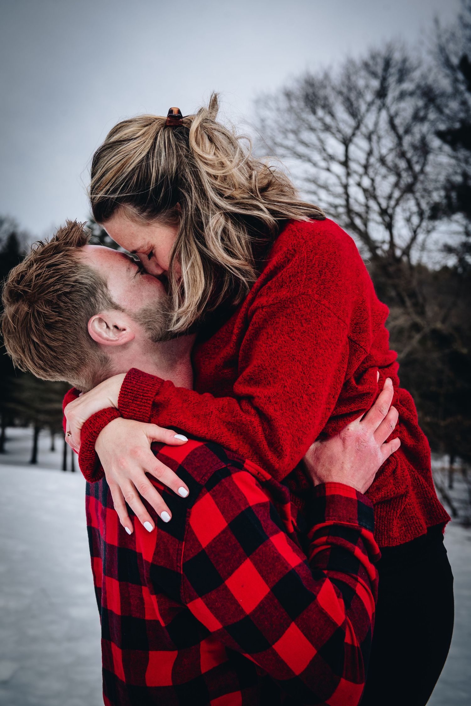A romantic embrace in the snow featuring red and black buffalo plaid. Massachusetts Engagement Photographer- Affordable