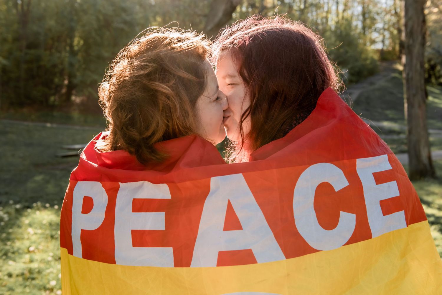 Two people wrapped in a pride PEACE flag sharing a tender moment outdoors. LGBT LGBTQ+ Friendly photographer