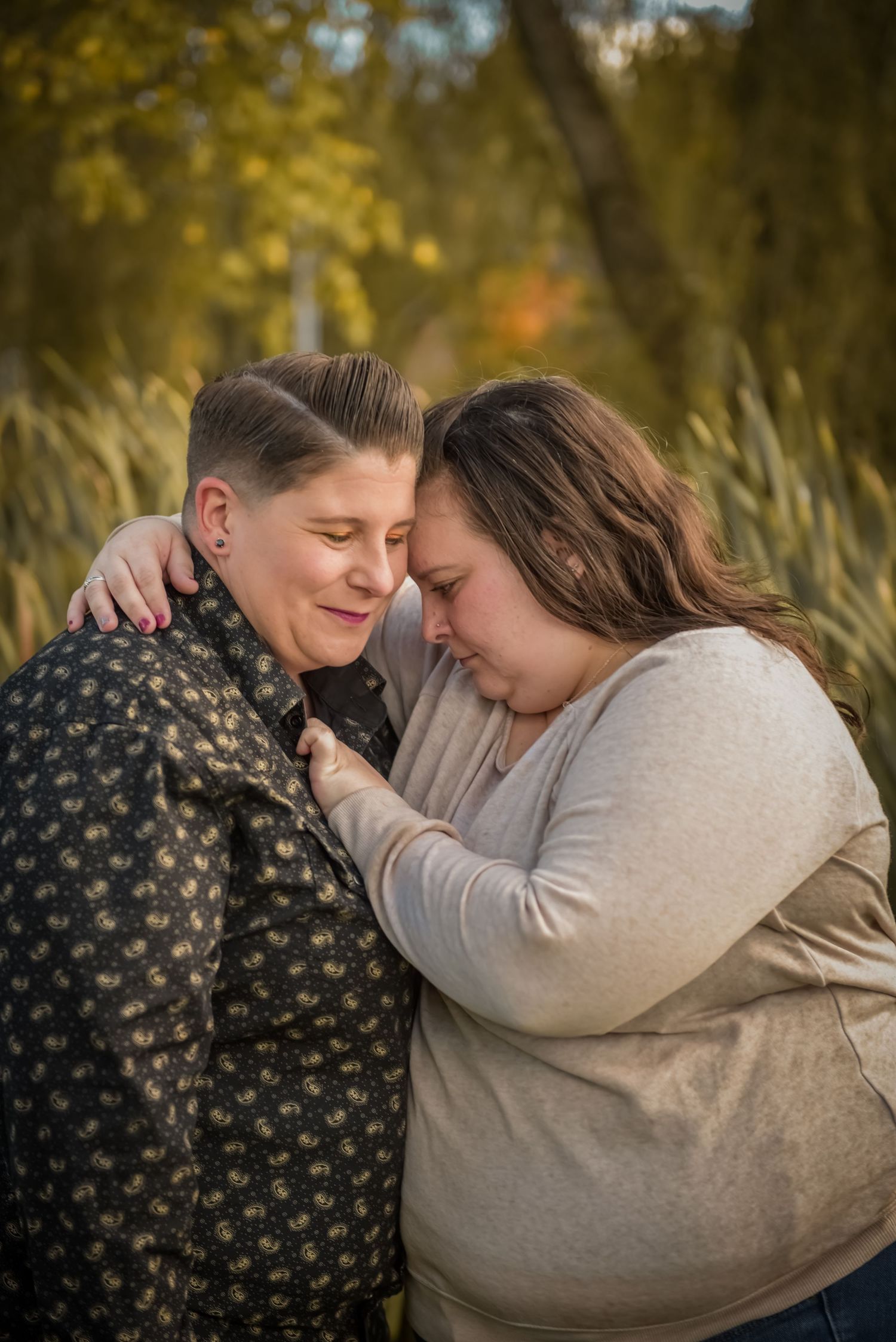 Tender moment between couple embracing outdoors with autumn foliage in background. LGBT LGBTQ+ Friendly photographer