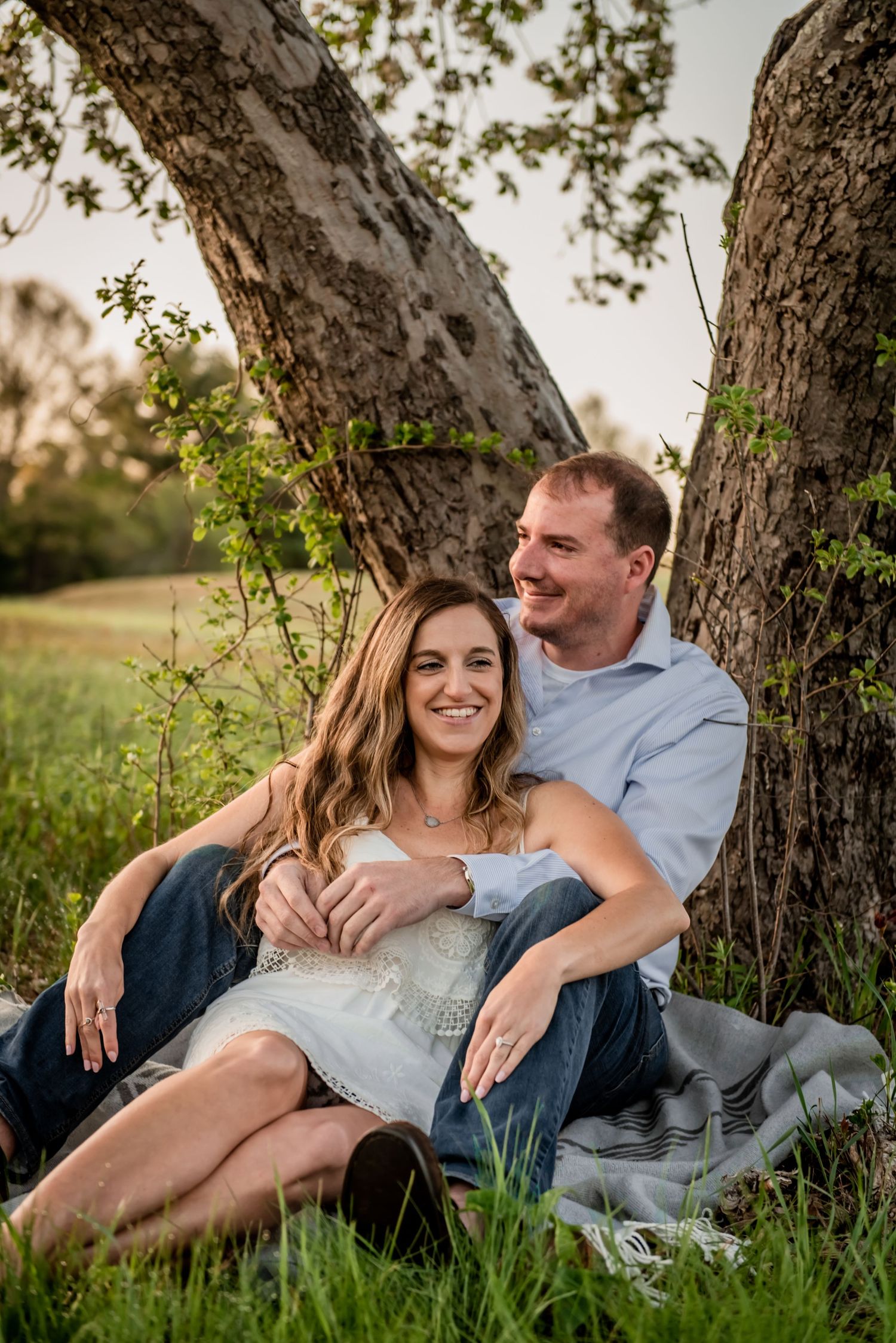 Relaxed couple lounging against tree trunk in natural setting at sunset. Massachusetts Engagement Photographer- Affordable