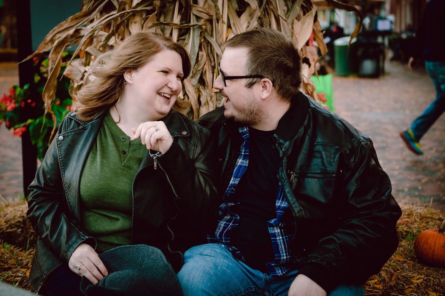 A couple laughing together while sitting among fall decorations. Massachusetts Engagement Photographer Serving the North Shore