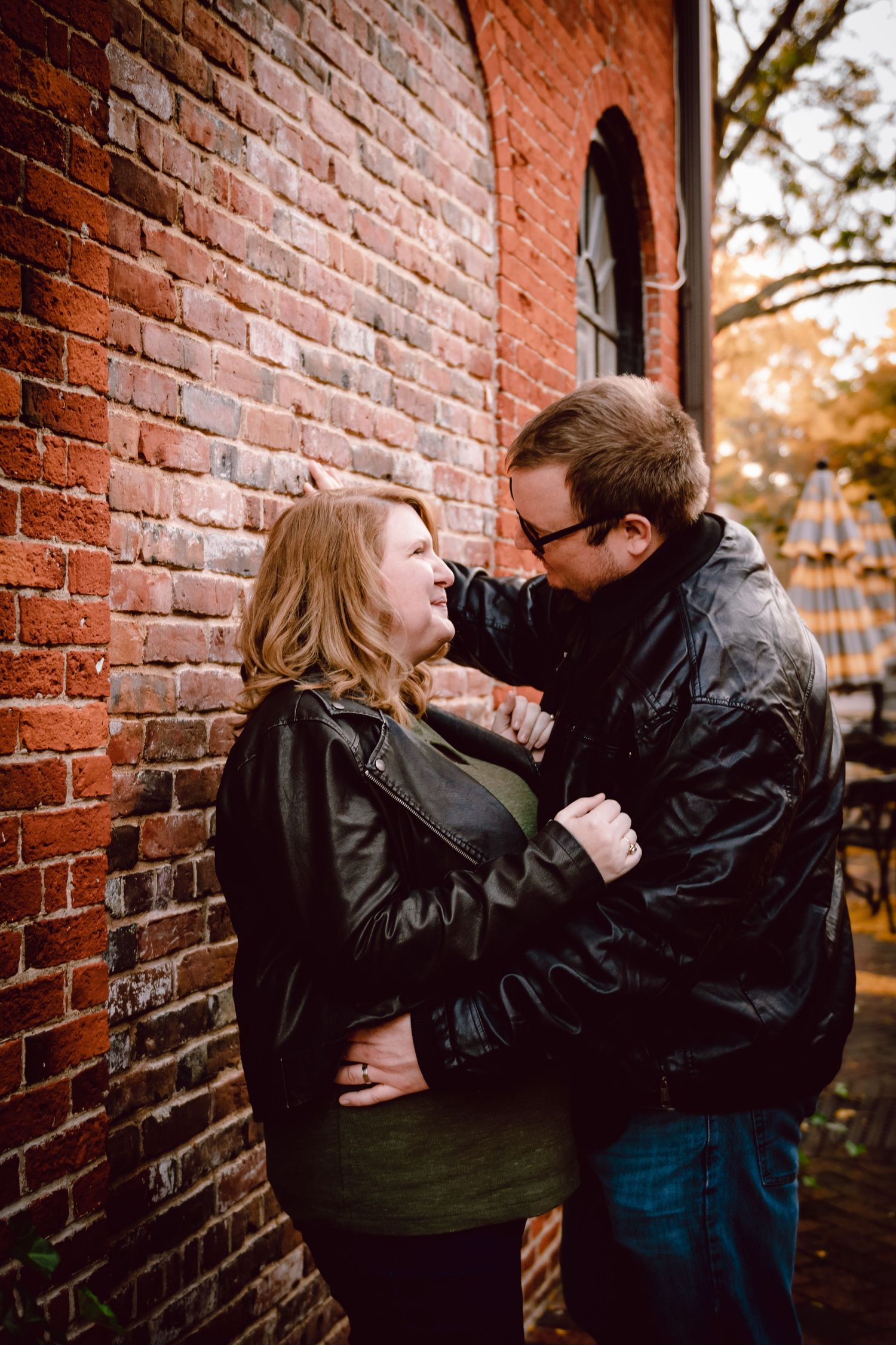A couple shares a playful moment against a rustic brick wall. Boston Engagement Photographer Serving New England