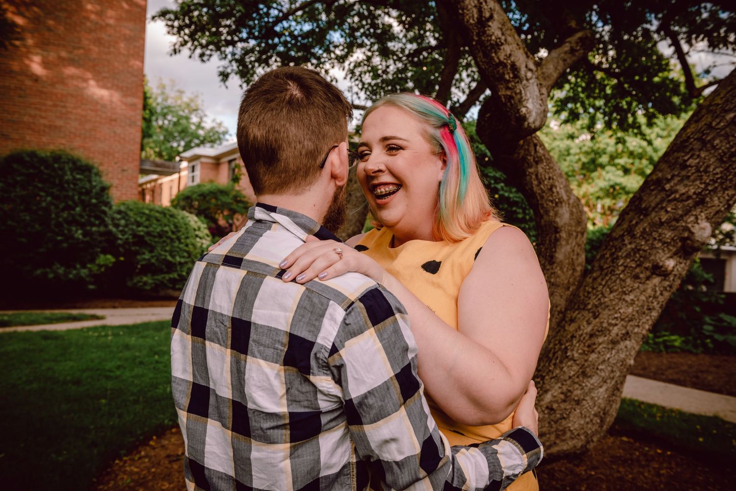Joyful moment shared between couple near tree in backyard setting. Massachusetts Engagement Photographer- Affordable