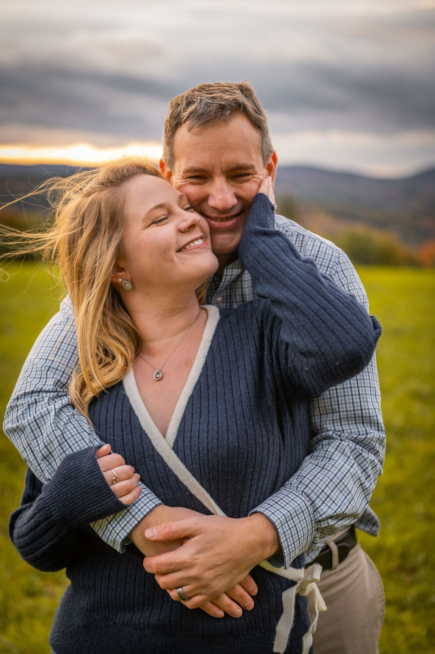 A romantic embrace on a hilltop during sunset with mountains in the background. New Hampshire Engagement Photos- Affordable