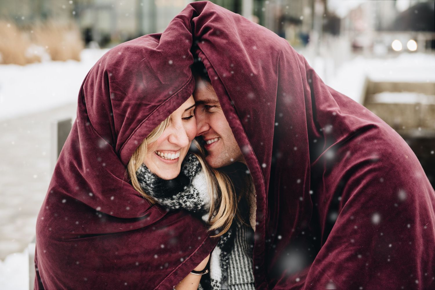 A cozy winter moment shared under a burgundy blanket during snowfall. Massachusetts Engagement Photographer Serving New England