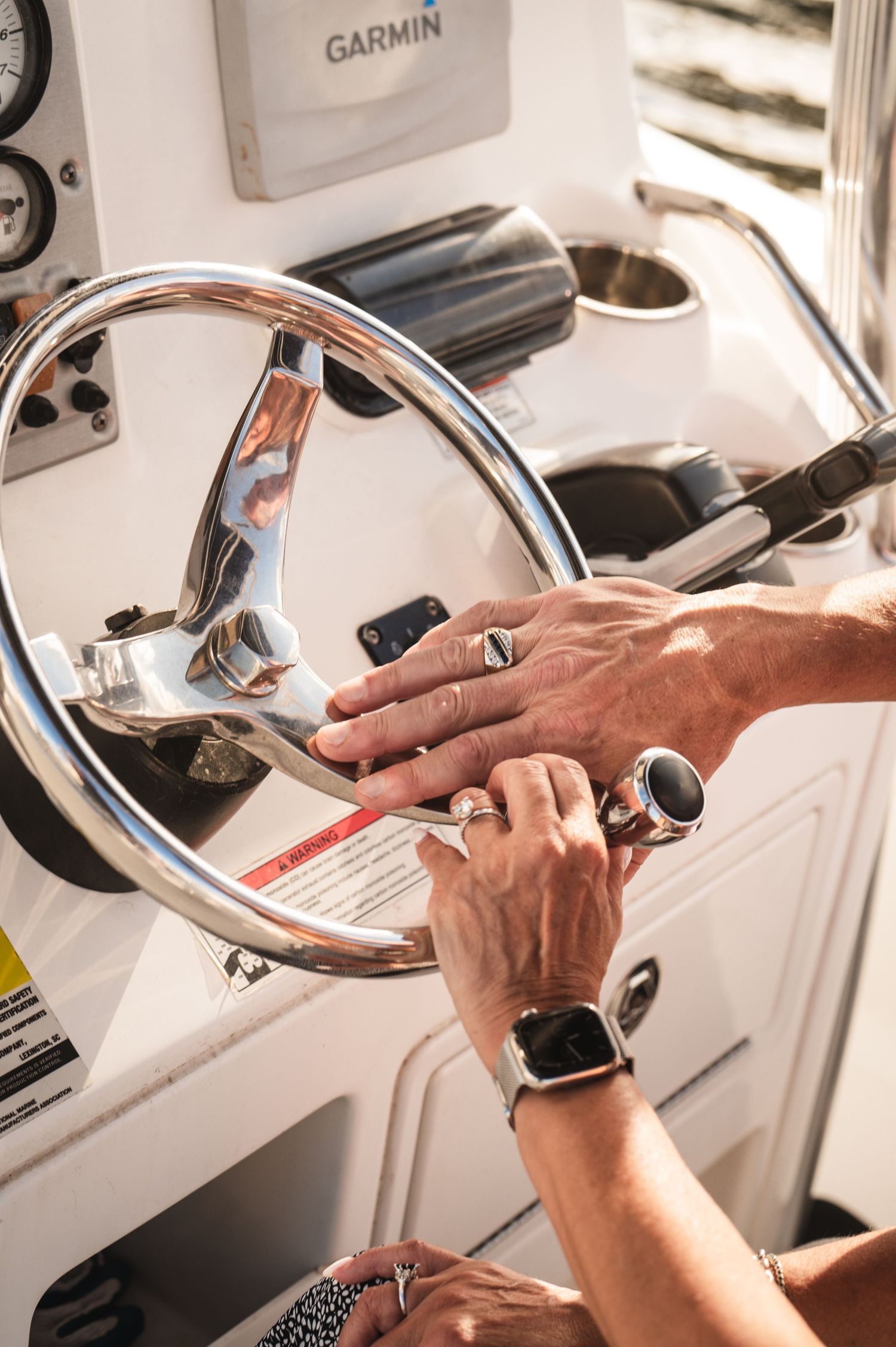 Hands gripping a chrome boat steering wheel with a Garmin device mounted in the background.