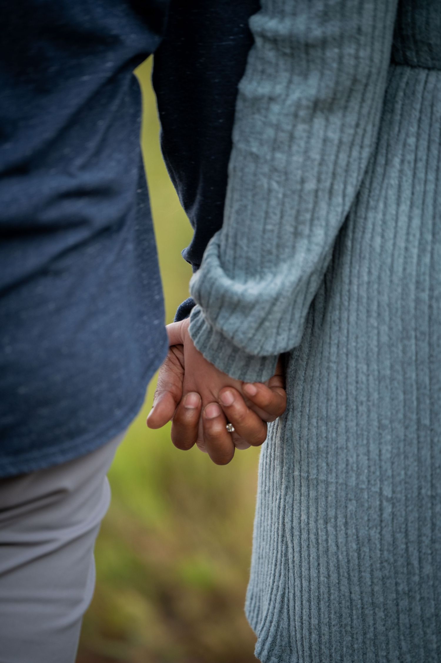 A close-up shot of two people holding hands against a blurred green natural background.