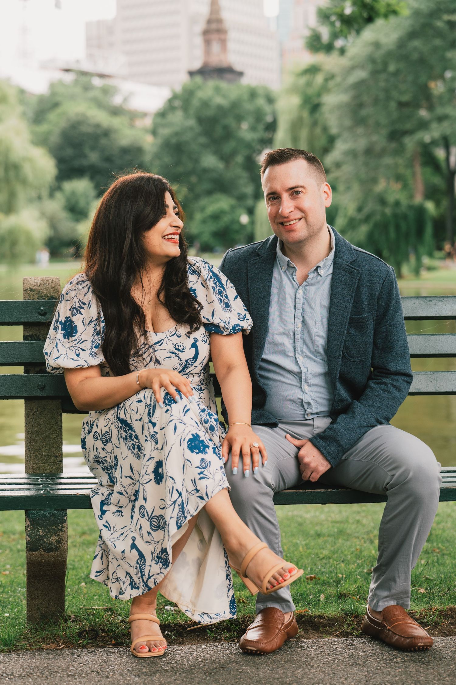 A couple sharing a candid laughing moment while sitting on a park bench. Boston Engagement & Wedding Photographer