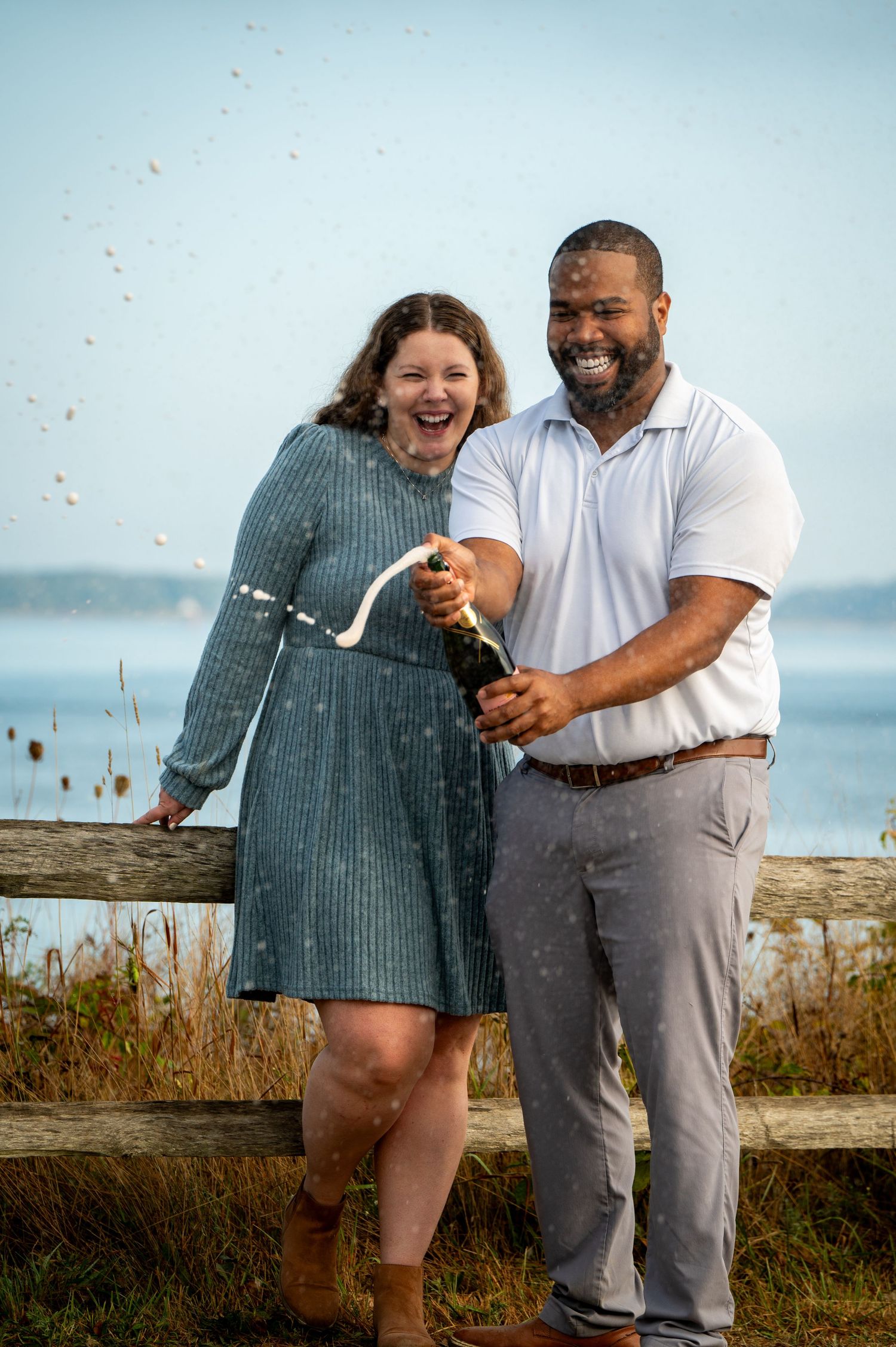 Happy couple sharing a joyful moment together while standing outdoors near the ocean on a sunny day.