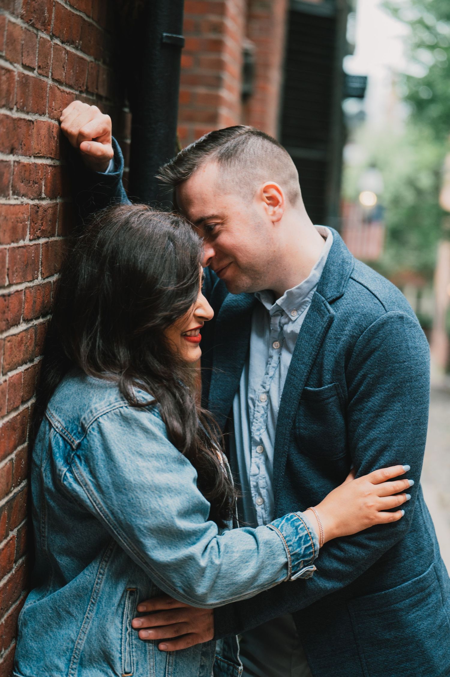 A romantic couple embracing against a brick wall in an urban setting. Boston Engagement & Wedding Photographer