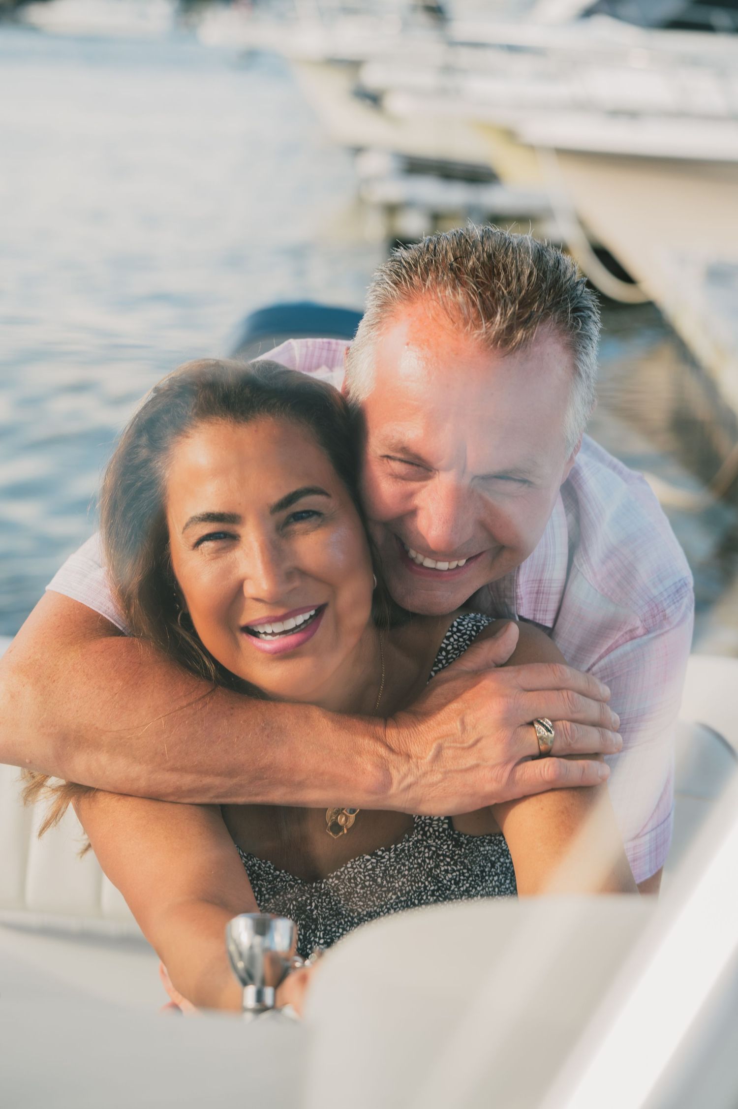 A happy couple smiles and embraces while sitting together on a boat in the water during golden hour.