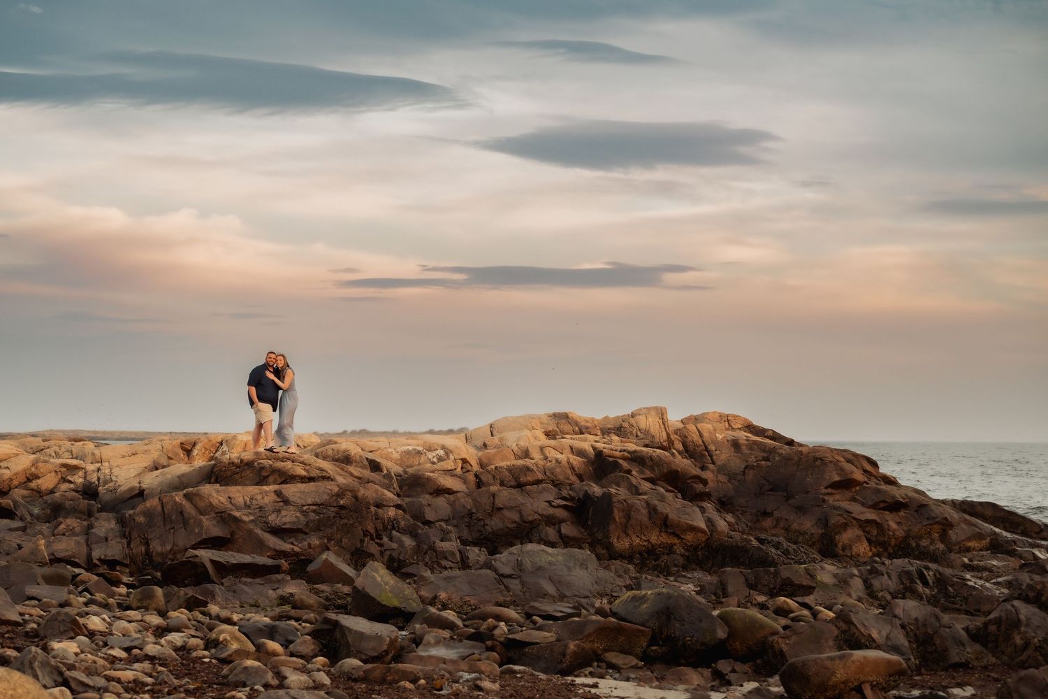 A silhouette stands atop rocky coastal cliffs against a dreamy pastel sunset sky over the ocean.