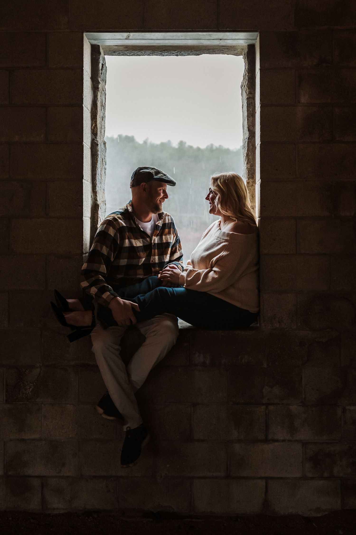A couple sits together in a window frame silhouetted against soft natural light, creating an intimate moment.