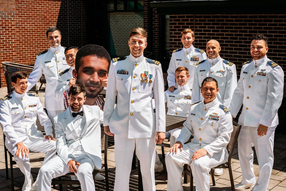 A group portrait of service members in white naval uniforms outdoors.